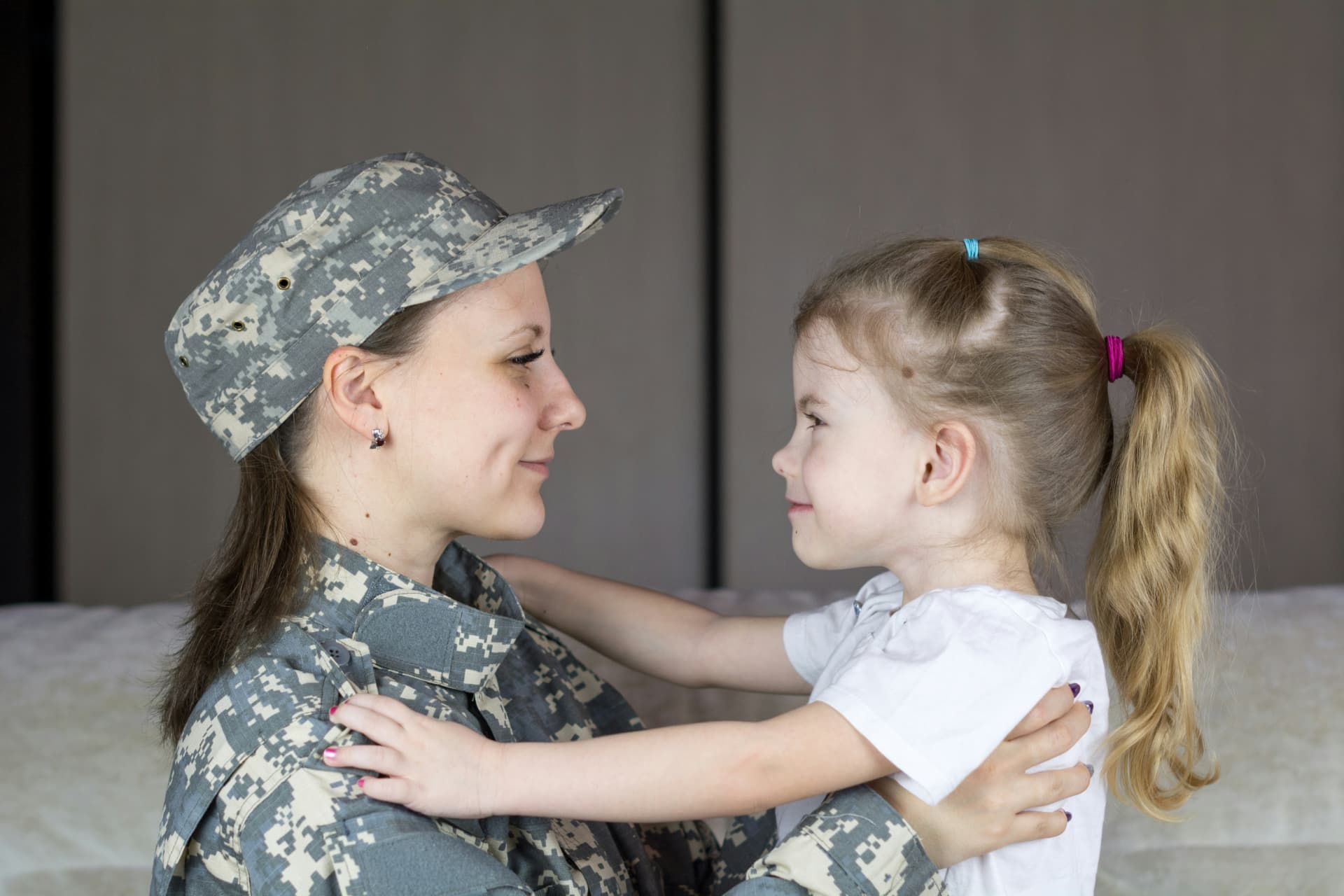 A service member in uniform smiling with her young daughter
